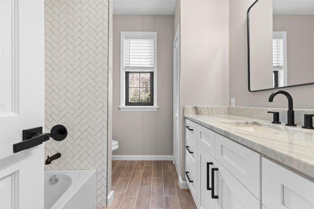 bathroom featuring wood finish floors, shower / bathing tub combination, toilet, vanity, and baseboards