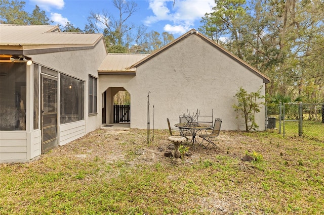 view of side of home with stucco siding, a lawn, a sunroom, metal roof, and fence