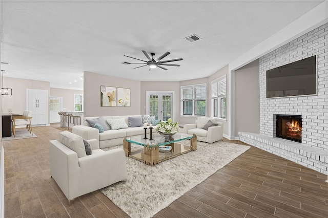 living area with a brick fireplace, wood tiled floor, visible vents, and ceiling fan