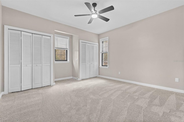 unfurnished bedroom with multiple closets, light carpet, baseboards, and a ceiling fan