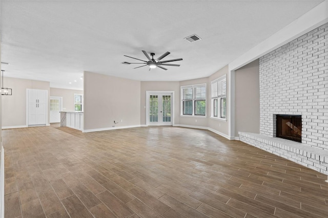 unfurnished living room with a ceiling fan, a brick fireplace, visible vents, and dark wood finished floors