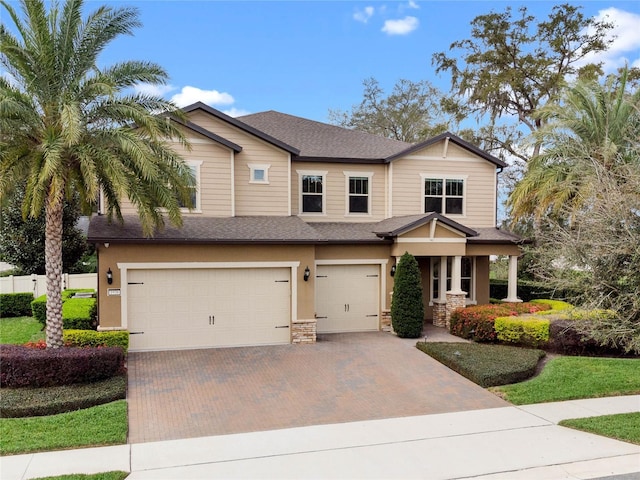 craftsman-style home featuring an attached garage, stone siding, roof with shingles, stucco siding, and decorative driveway