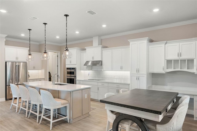 kitchen with light countertops, appliances with stainless steel finishes, a kitchen breakfast bar, white cabinetry, and an island with sink