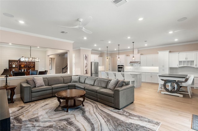 living area featuring stairs, ceiling fan with notable chandelier, visible vents, and light wood finished floors