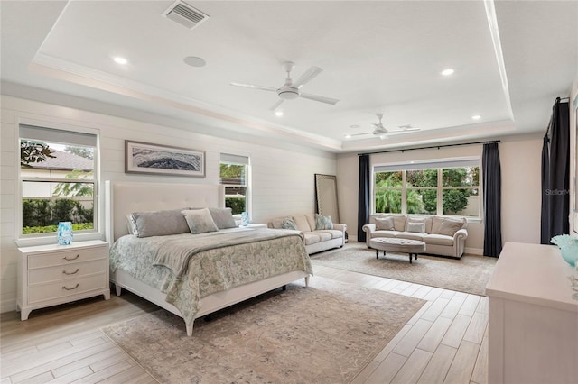 bedroom featuring multiple windows, visible vents, light wood-style floors, and a tray ceiling