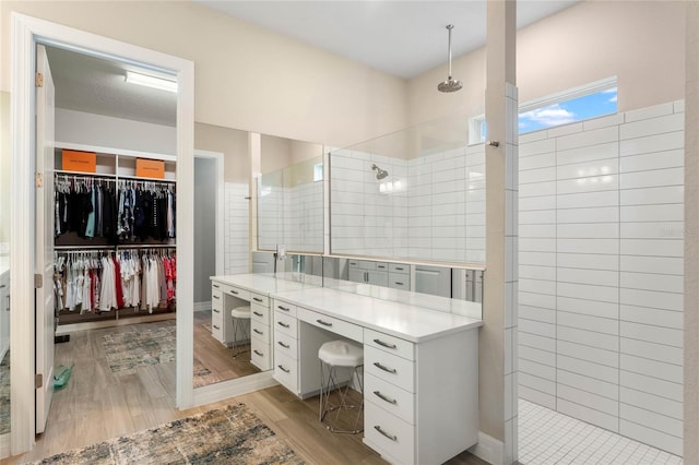 bathroom featuring wood finished floors, vanity, a spacious closet, and a walk in shower