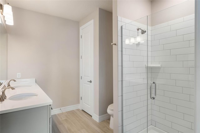 bathroom with double vanity, toilet, a tile shower, baseboards, and wood finished floors