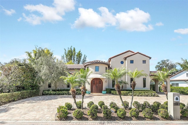 mediterranean / spanish-style home with a tiled roof, decorative driveway, and stucco siding