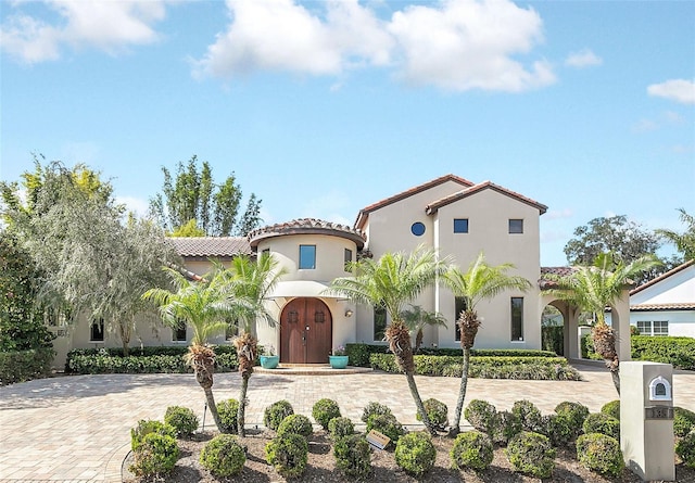 mediterranean / spanish house with decorative driveway, a tiled roof, and stucco siding