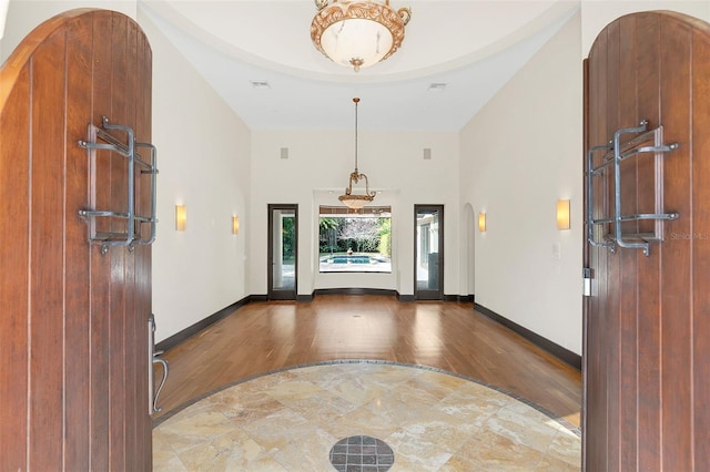 foyer entrance with arched walkways, high vaulted ceiling, wood finished floors, and baseboards