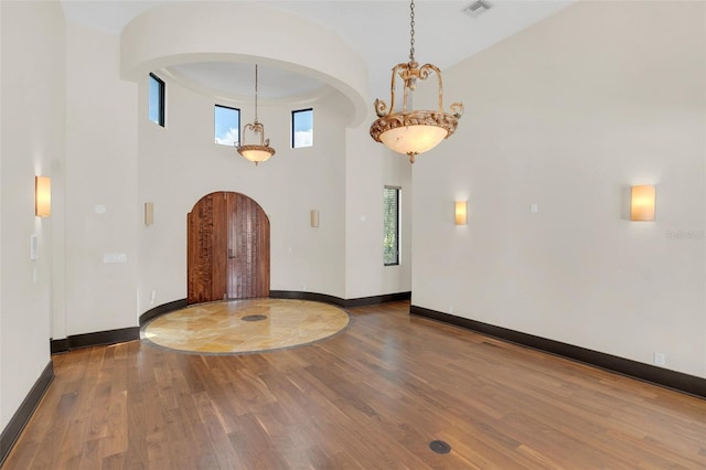 entryway with baseboards, visible vents, arched walkways, wood finished floors, and a high ceiling