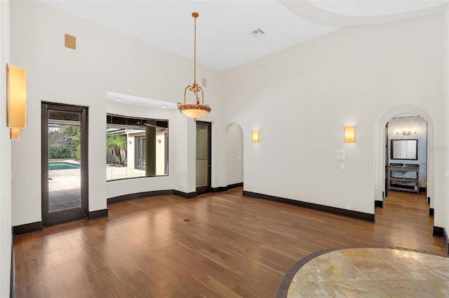 unfurnished living room featuring arched walkways, visible vents, wood finished floors, high vaulted ceiling, and baseboards