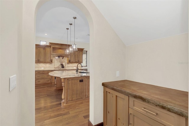 kitchen featuring arched walkways, hanging light fixtures, backsplash, light wood-style floors, and a sink