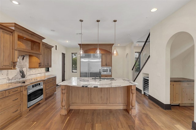 kitchen featuring wood finished floors, an island with sink, decorative backsplash, and built in appliances