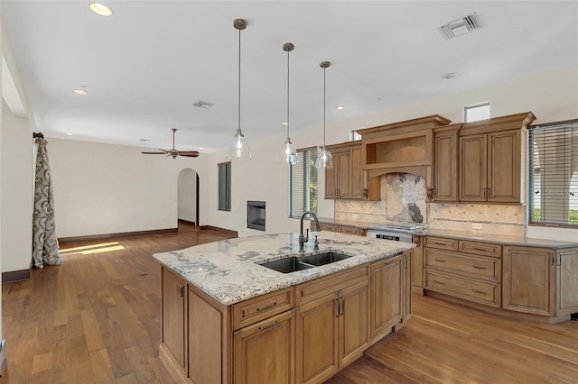 kitchen featuring visible vents, arched walkways, a sink, premium range hood, and backsplash