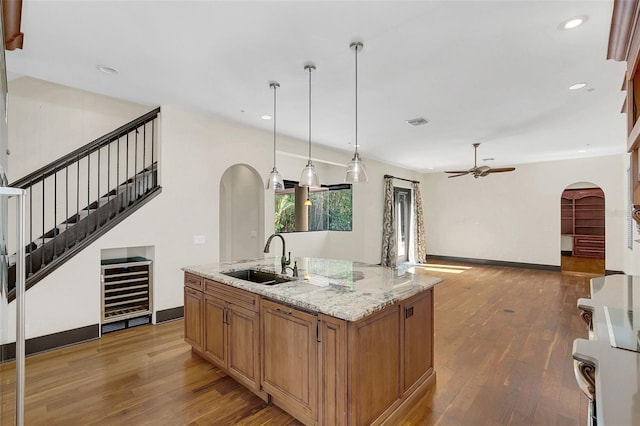 kitchen with arched walkways, wine cooler, a sink, and hardwood / wood-style flooring