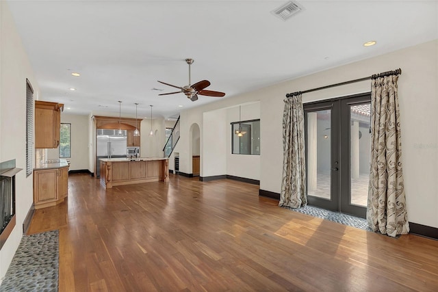 unfurnished living room featuring dark wood-style floors, arched walkways, french doors, visible vents, and baseboards