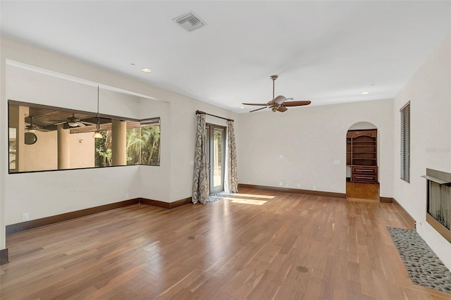 unfurnished living room featuring arched walkways, wood finished floors, visible vents, and baseboards