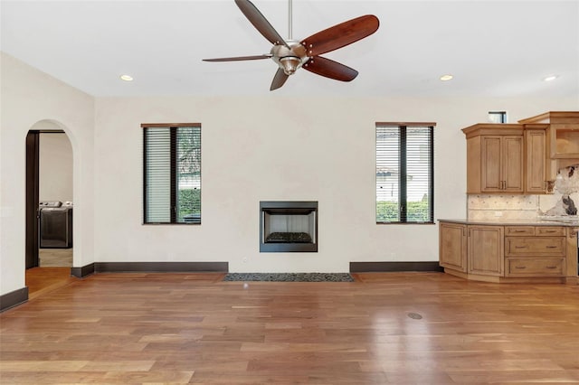 unfurnished living room with arched walkways, baseboards, a fireplace with flush hearth, light wood-type flooring, and recessed lighting