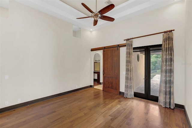 unfurnished bedroom with access to outside, wood finished floors, a tray ceiling, and a barn door