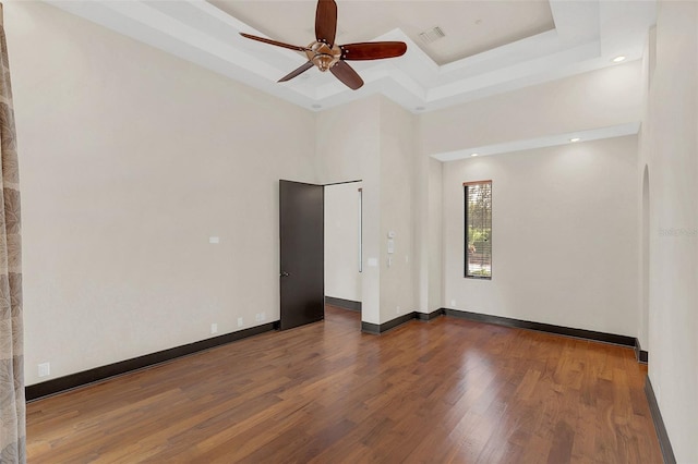 spare room featuring a tray ceiling, visible vents, baseboards, and wood finished floors