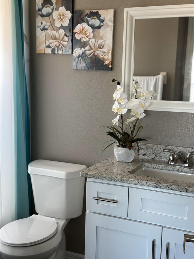 bathroom with a textured wall, vanity, and toilet