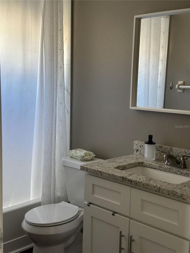 full bath with a textured wall, shower / bath combo with shower curtain, vanity, and toilet