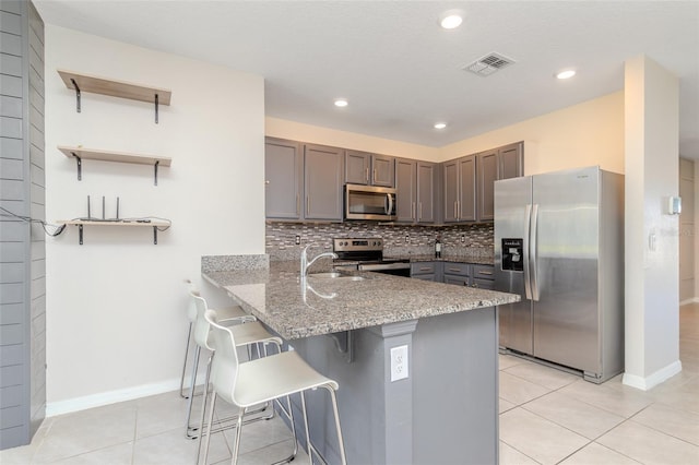 kitchen with a breakfast bar area, stainless steel appliances, light stone countertops, decorative backsplash, and kitchen peninsula