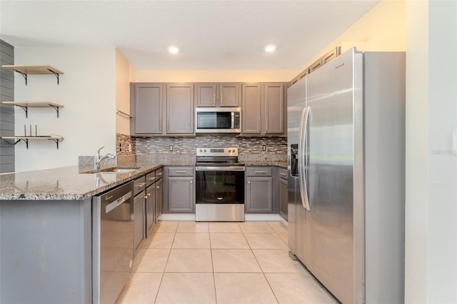 kitchen with gray cabinetry, appliances with stainless steel finishes, kitchen peninsula, and dark stone countertops