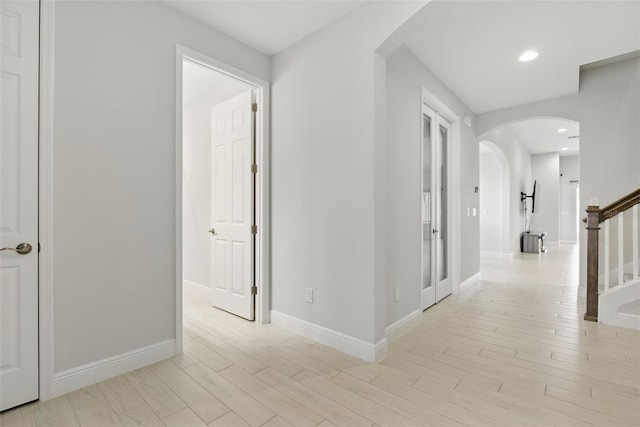 hallway featuring light wood-type flooring, stairs, arched walkways, and recessed lighting