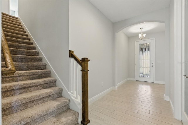 foyer entrance with light wood finished floors, baseboards, arched walkways, stairs, and a chandelier