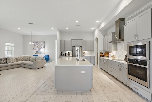 kitchen with appliances with stainless steel finishes, gray cabinets, open floor plan, and wall chimney exhaust hood