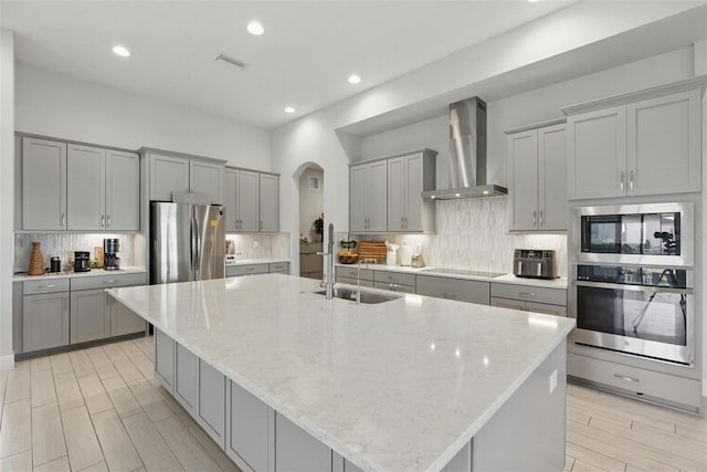 kitchen featuring appliances with stainless steel finishes, arched walkways, gray cabinets, and wall chimney range hood