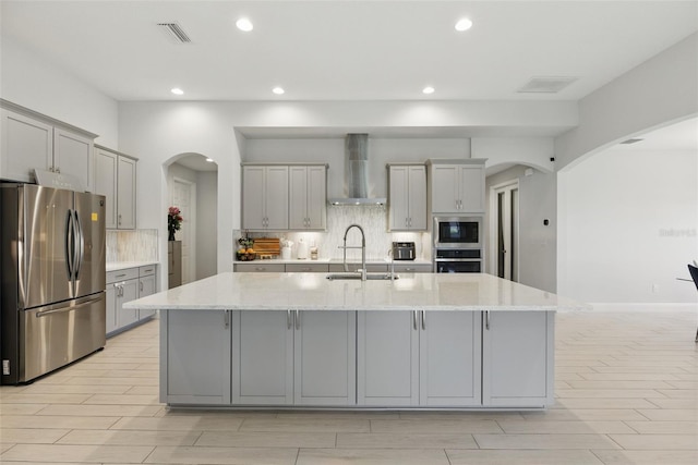 kitchen with gray cabinetry, stainless steel appliances, a sink, visible vents, and wall chimney range hood