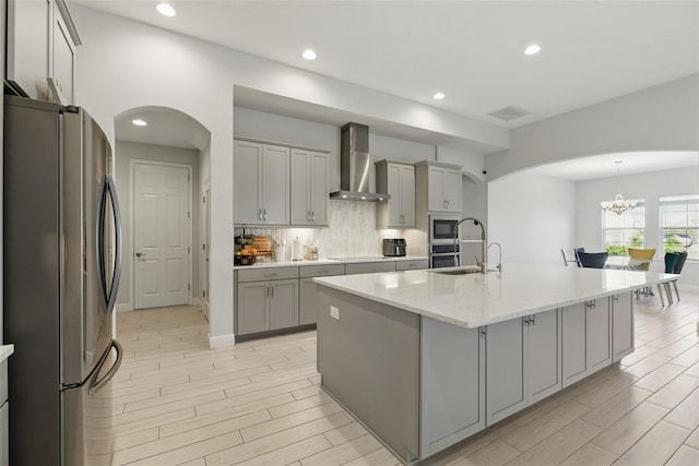 kitchen featuring appliances with stainless steel finishes, arched walkways, gray cabinets, and wall chimney range hood