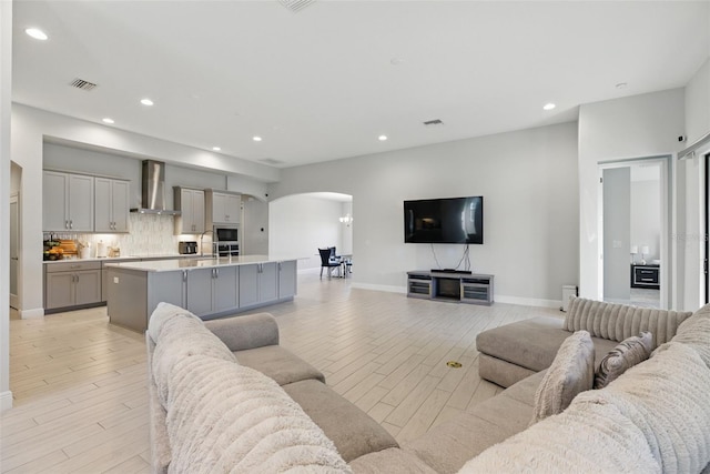 living area featuring light wood finished floors, baseboards, visible vents, arched walkways, and recessed lighting