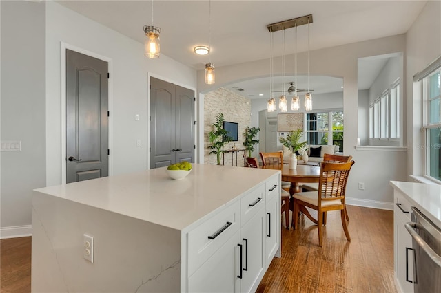 kitchen featuring arched walkways, dishwashing machine, a kitchen island, wood finished floors, and light countertops