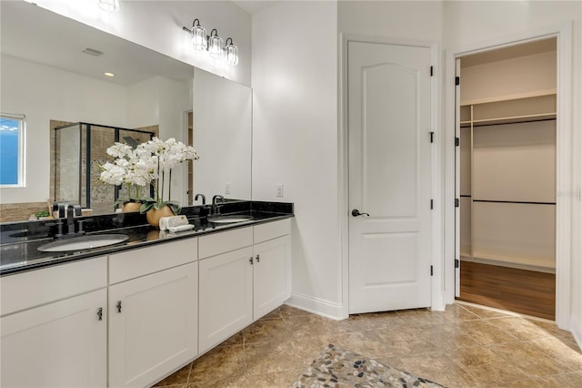 bathroom featuring a stall shower, a walk in closet, a sink, and double vanity