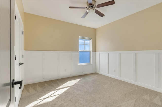 empty room featuring a ceiling fan, a wainscoted wall, light colored carpet, and a decorative wall