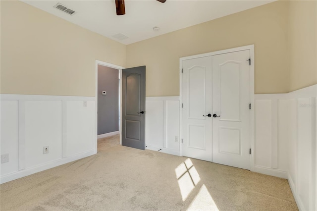 unfurnished bedroom with light carpet, visible vents, a decorative wall, and a closet