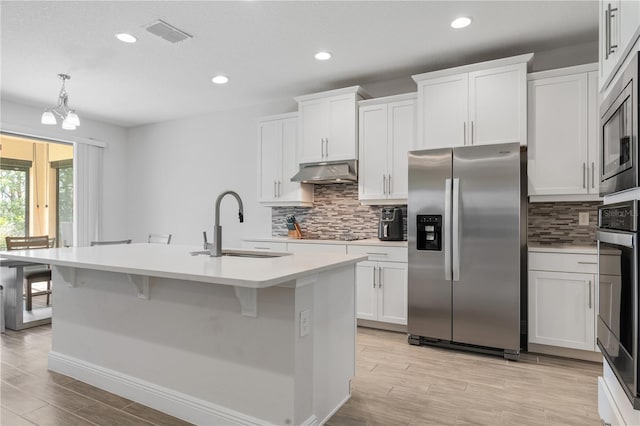 kitchen with stainless steel appliances, pendant lighting, a center island with sink, and white cabinets