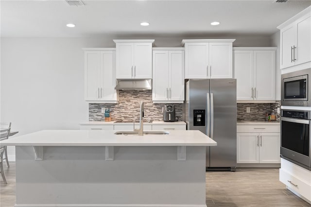 kitchen featuring appliances with stainless steel finishes, a center island with sink, white cabinets, and a kitchen bar