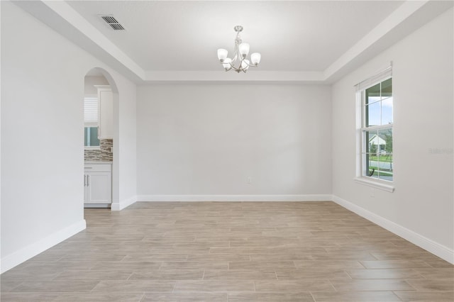 spare room featuring a raised ceiling, a chandelier, and light wood-type flooring