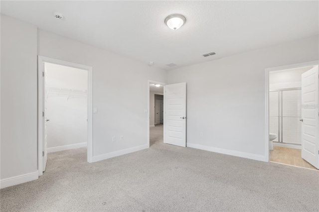 unfurnished bedroom featuring a spacious closet, light colored carpet, a closet, and ensuite bathroom