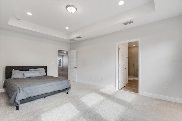 bedroom with a tray ceiling, ensuite bathroom, and carpet flooring