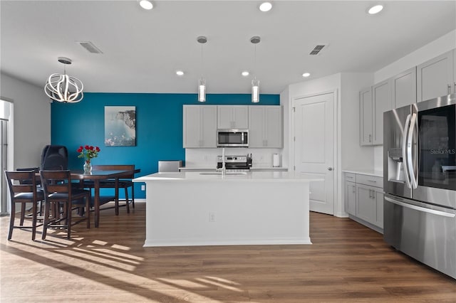 kitchen with sink, hanging light fixtures, dark hardwood / wood-style floors, stainless steel appliances, and a kitchen island with sink