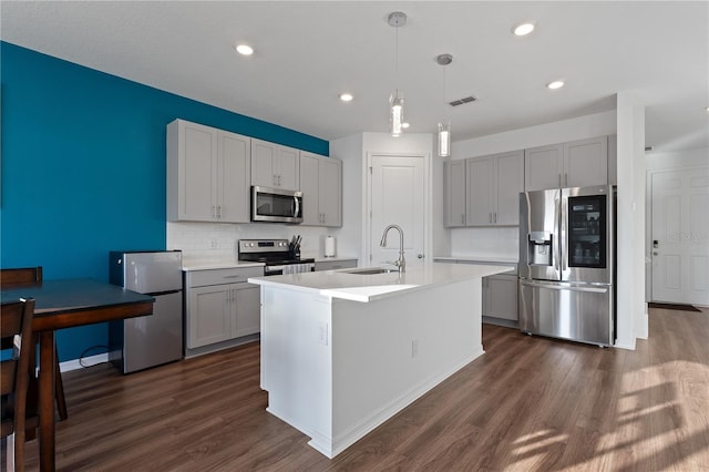 kitchen featuring gray cabinets, an island with sink, sink, hanging light fixtures, and stainless steel appliances