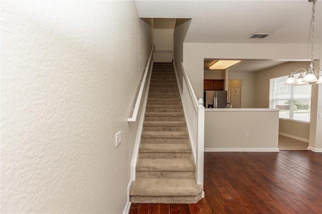 stairway featuring an inviting chandelier and wood-type flooring