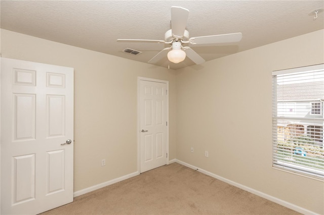 unfurnished bedroom with ceiling fan, light carpet, and a textured ceiling