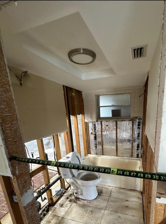 bathroom with bathtub / shower combination, a raised ceiling, and toilet